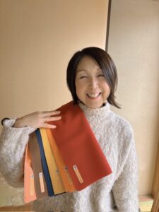 パーソナルカラー診断でイエベ秋タイプのカラードレープを持ち、笑顔でポーズをとるお客様。深みのあるオレンジやブラウンなど、オータムカラーが似合う事例。