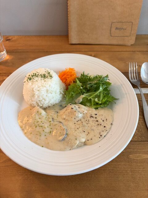 大倉山のカフェランチ。白いお皿に盛られたクリームシチューとライス、サラダのワンプレート。木のテーブルにナチュラルな雰囲気で提供されている一人ランチの様子。