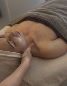 ベッドに横たわるお客様の背面からデコルテにかけて、スウェディッシュマッサージを行っている施術シーン。 首・肩・背中の筋肉（僧帽筋や広背筋など）にやさしくアプローチしながら、血流やリンパの巡りを整え、フェイシャルの効果を引き出すための土台を整えている様子。 ほうれい線やたるみの原因となる身体の緊張をゆるめる、irokaの施術の一場面。