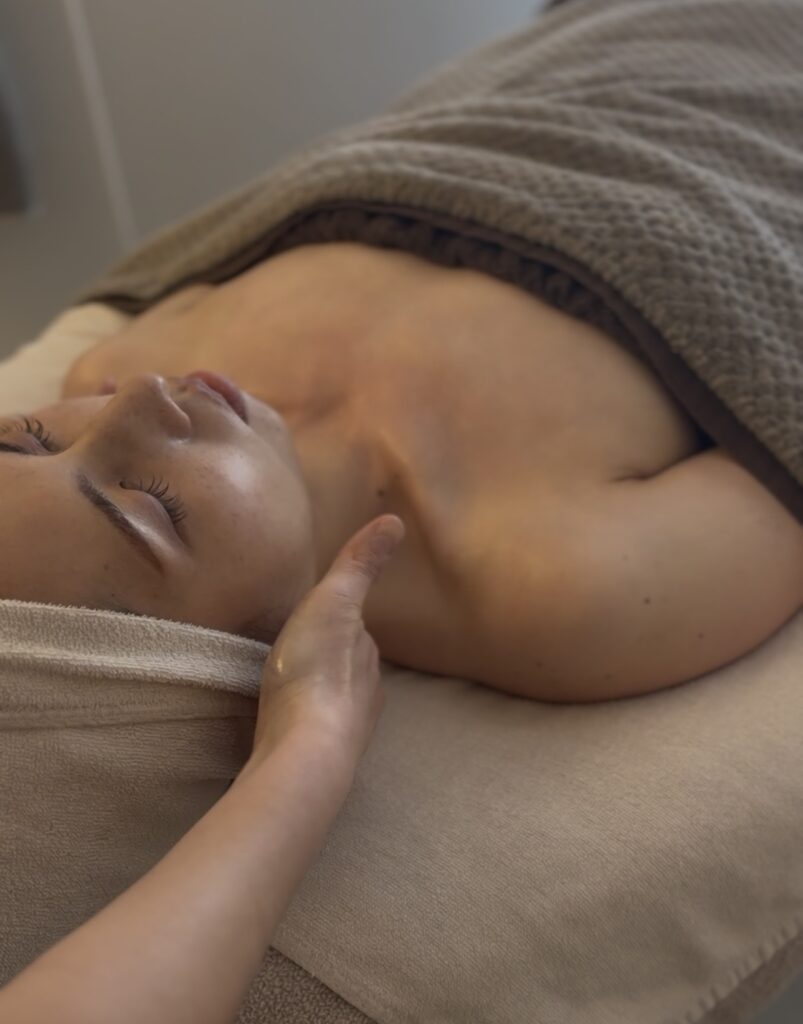 ベッドに横たわるお客様の背面からデコルテにかけて、スウェディッシュマッサージを行っている施術シーン。 首・肩・背中の筋肉（僧帽筋や広背筋など）にやさしくアプローチしながら、血流やリンパの巡りを整え、フェイシャルの効果を引き出すための土台を整えている様子。 ほうれい線やたるみの原因となる身体の緊張をゆるめる、irokaの施術の一場面。