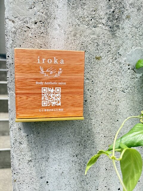 横浜市鶴見区のプライベートサロン「iroka」の木製看板。スウェディッシュマッサージとフェイシャルを提供する完全予約制サロンの入口に設置されたQRコード付き看板。