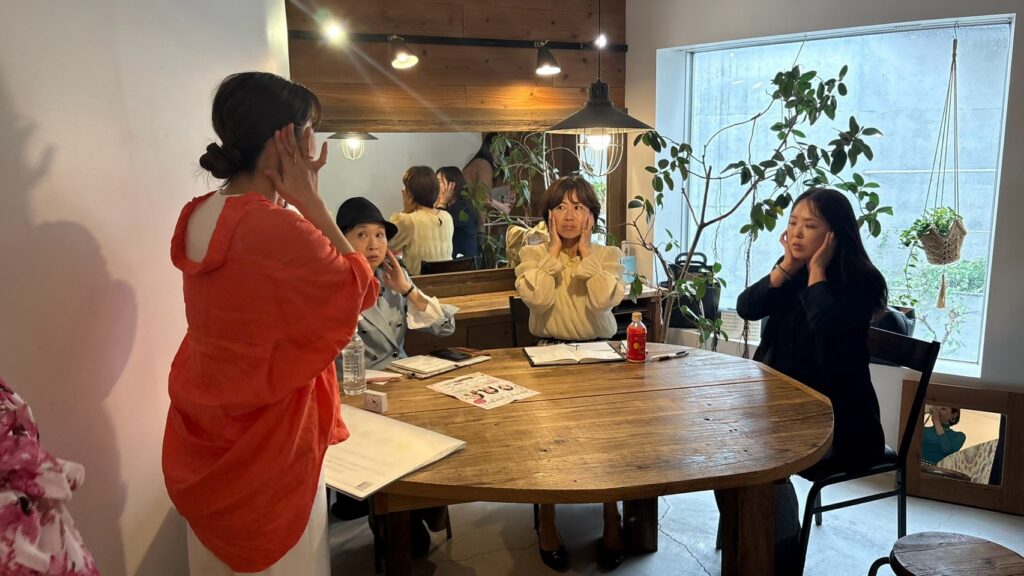 横浜市港北区・大倉山で開催された「THE HEROINE PROJECT」1DAY講座。イメージコンサルタント齋藤幸枝が、顔タイプ診断をもとに顔立ちの特徴や似合うメイクについて解説。参加者が実際に顔に手を当てながら学んでいる様子。